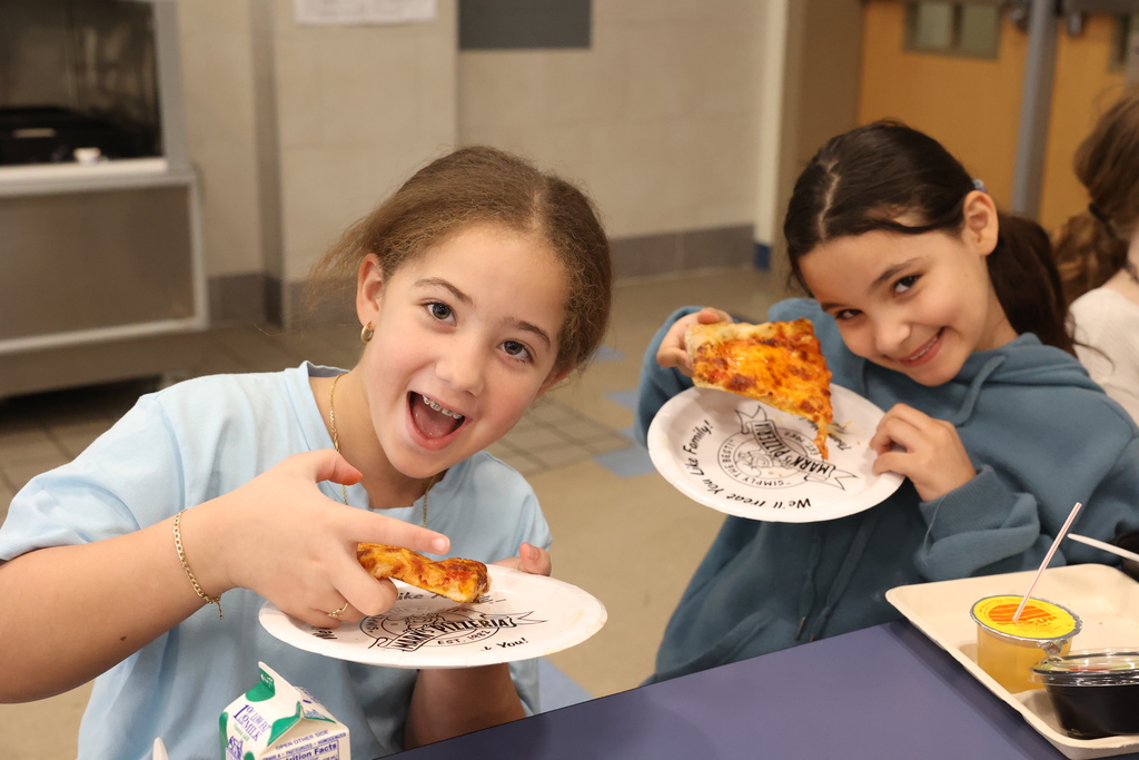 two students hold pizza and plates and smile for their pizza celebration