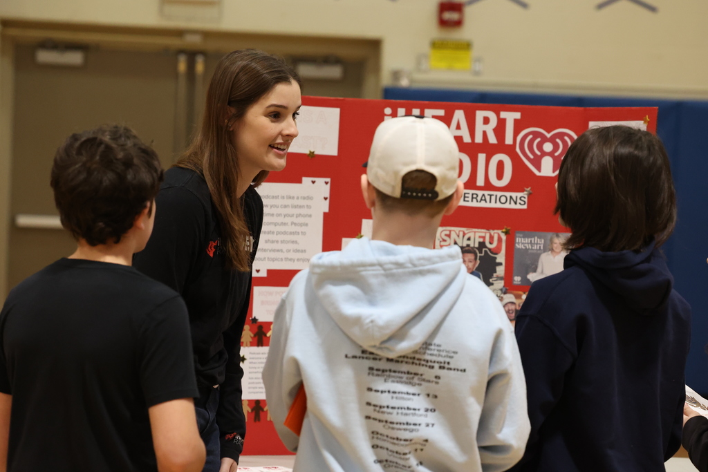 students talk to I Heart Radio rep with a poster board set up