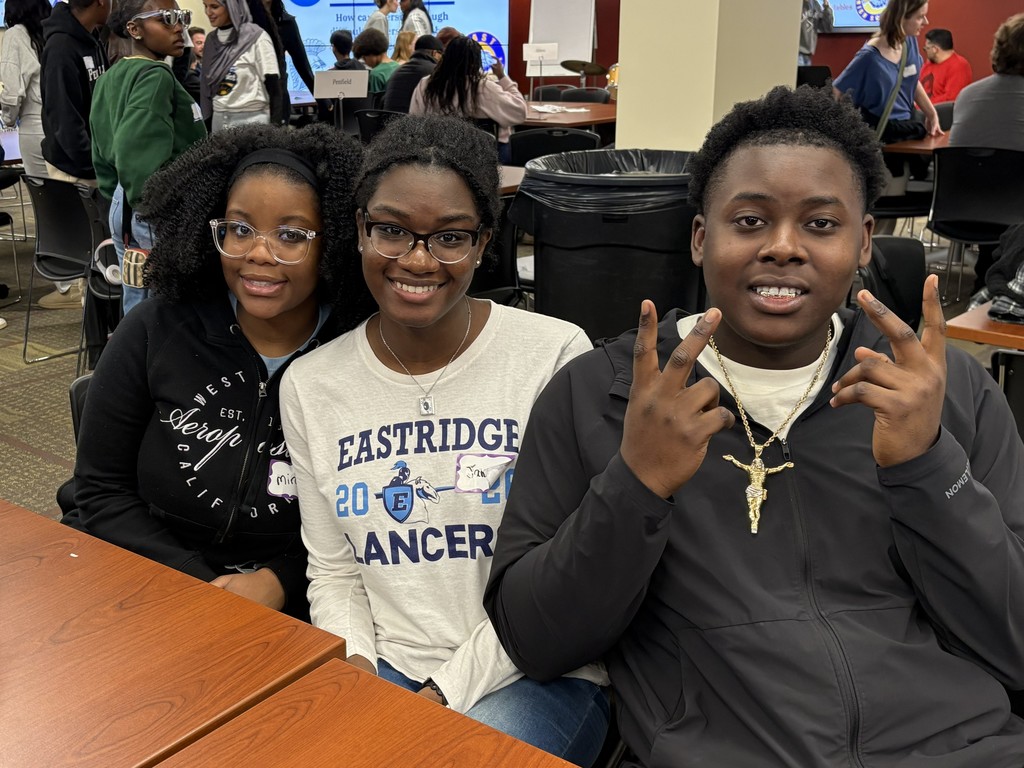 3 students wearing black sweatshirts and an eastridge shirt pose for a photo while sitting at a table at ROC2CHANGE