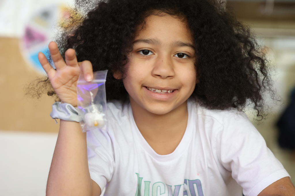 Student holds up clear bag with cotton ball and popcorn kernel and smiles
