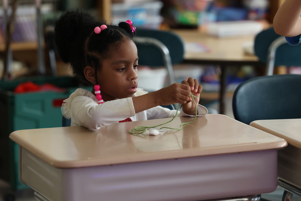 student works on tying her necklace