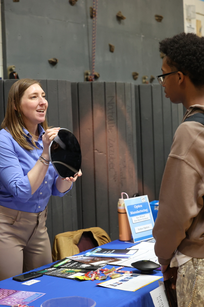 student talks to career fair visitor while she holds up mirror and discusses company
