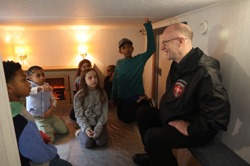 Irondequoit fire departments sits and talks to students in fake house about fire safety