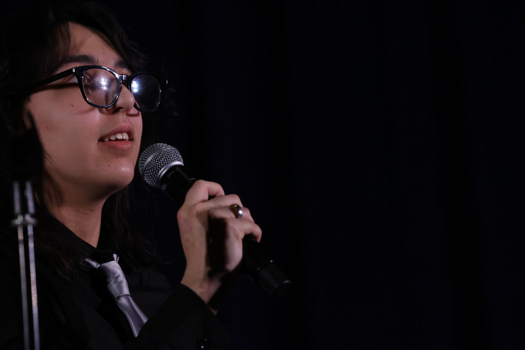 Singer holds mic and looks up with glasses 