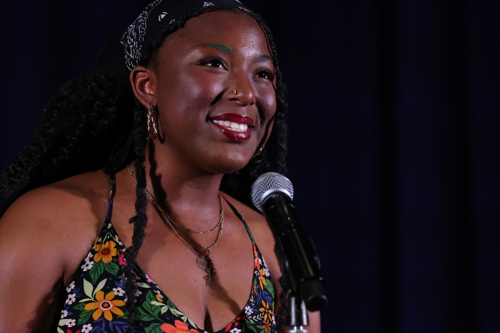 singer smiles on stage with mic stand while wearing flower dress