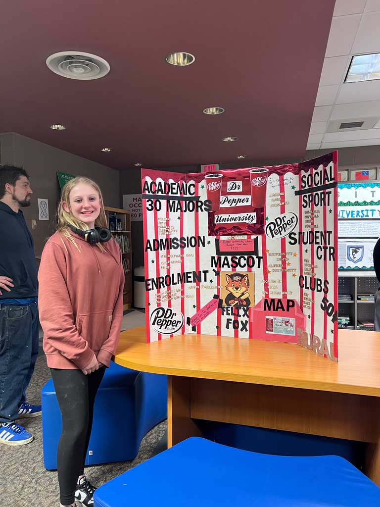 student stands with presentation board called Dr Pepper University 