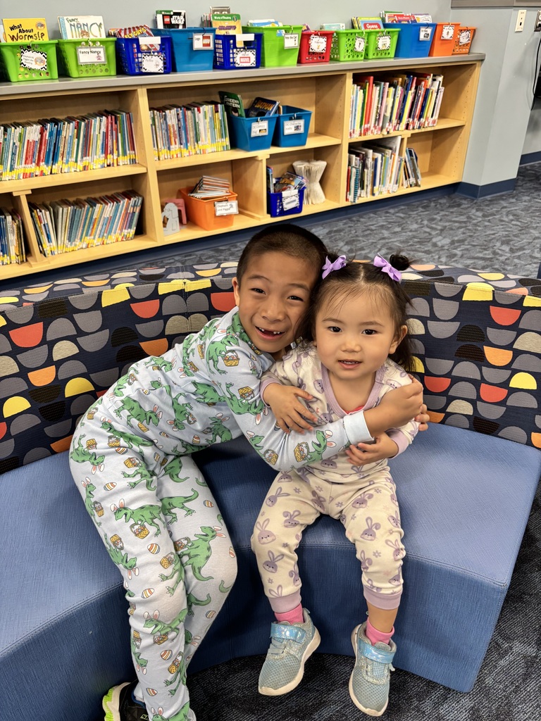 two students in their pjs smile for the camera in the library