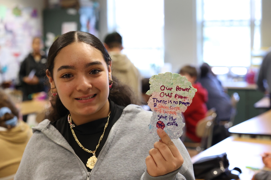 Student holds up piece of paper she created that says our power our planet there is no planet b small steps big impact save the earth