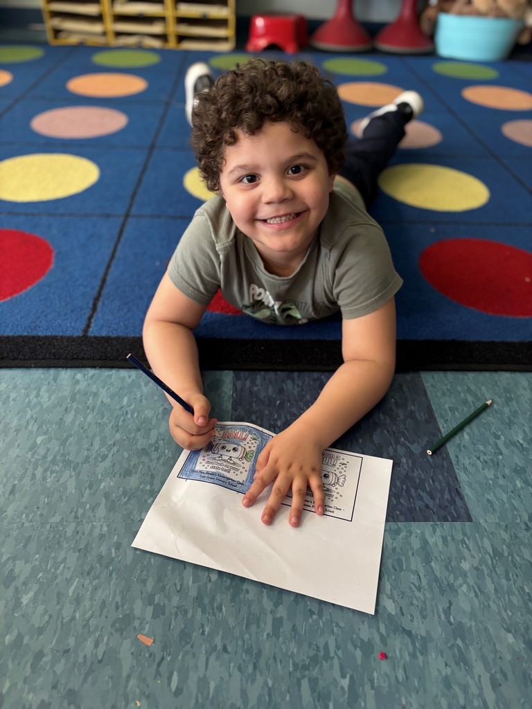 student smiles and colors card while laying on the carpet