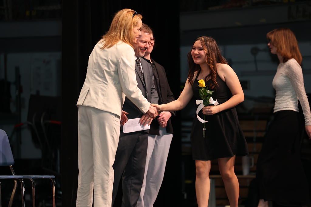 student shakes superintendent's hand with flower in her hand on stage