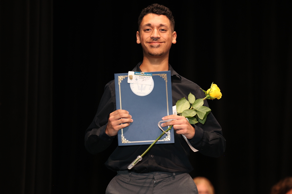student holds up certificate and flower for a photo on stage