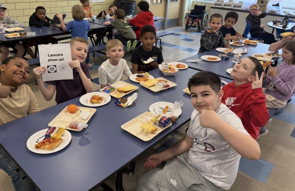 Ms Proctor class poses for attendance party eating pizza and holding up lancers show u psign