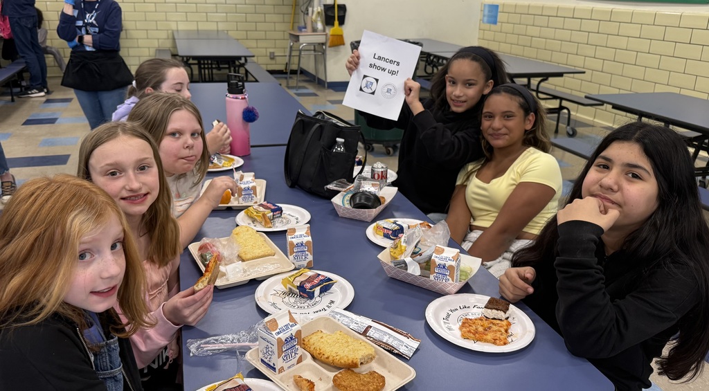 Ms Proctor class poses for attendance party eating pizza and holding up lancers show u psign