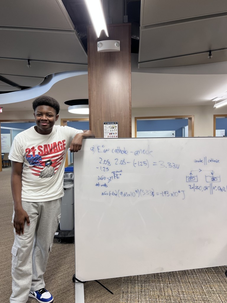 student stands by board with equation on it and smiles