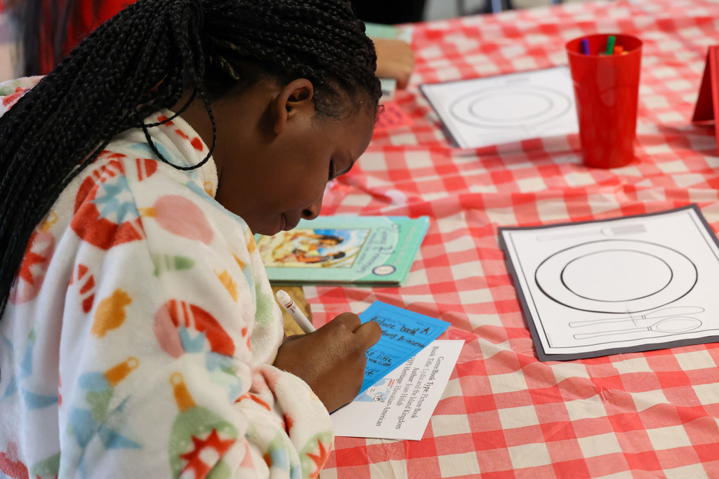 Student writes on worksheet while examining book