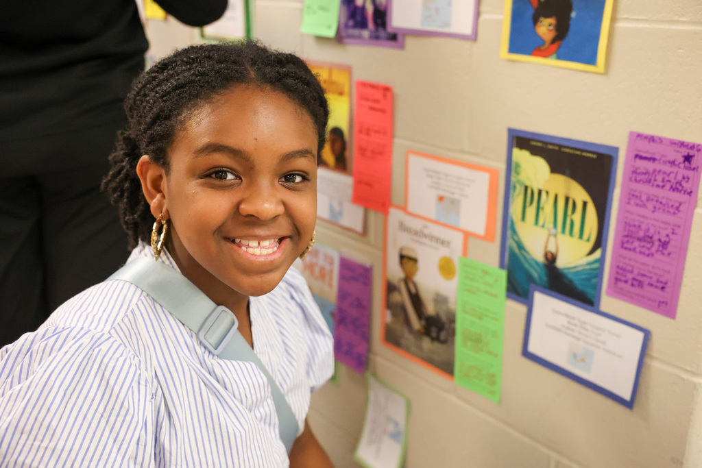 student smiles while next to wall display with books