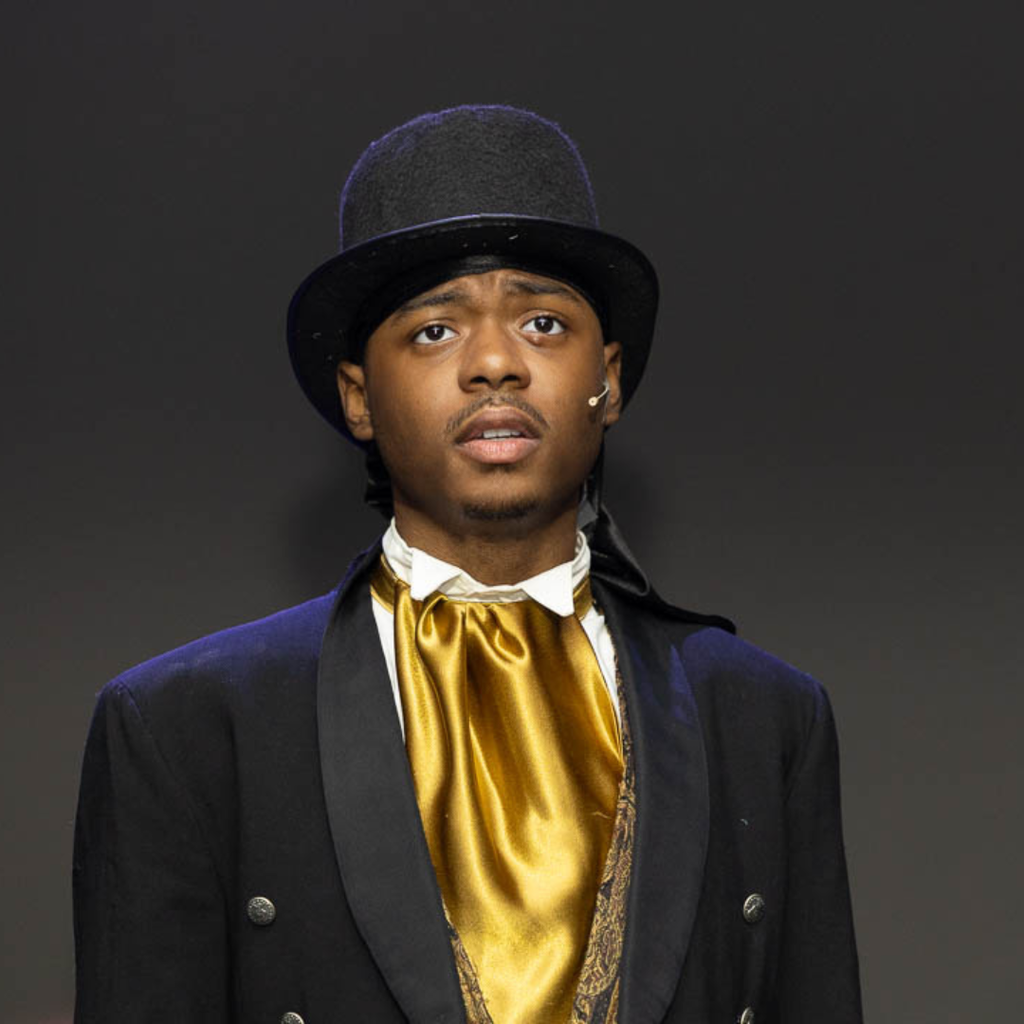 Students sings in a suit jacket, top hat with gold tie on stage during a performance of Les Mis