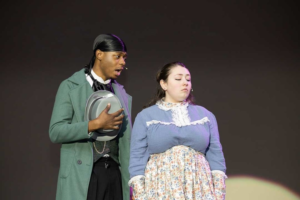 Singer sings to other performer with hat in his hands in green jacket