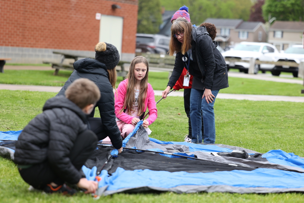 student helps slide rod into tent with her class