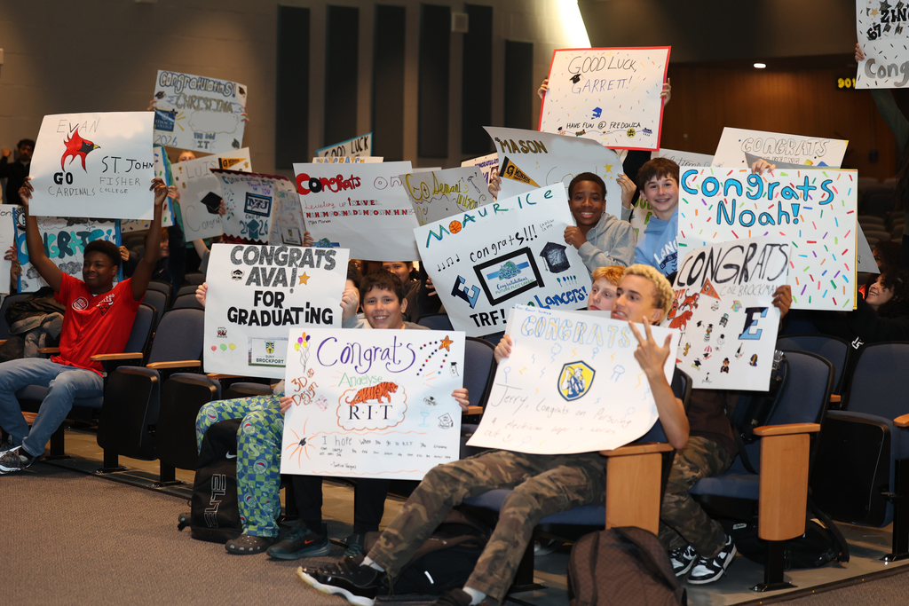 Students hold up posters and cheer on graduating seniors