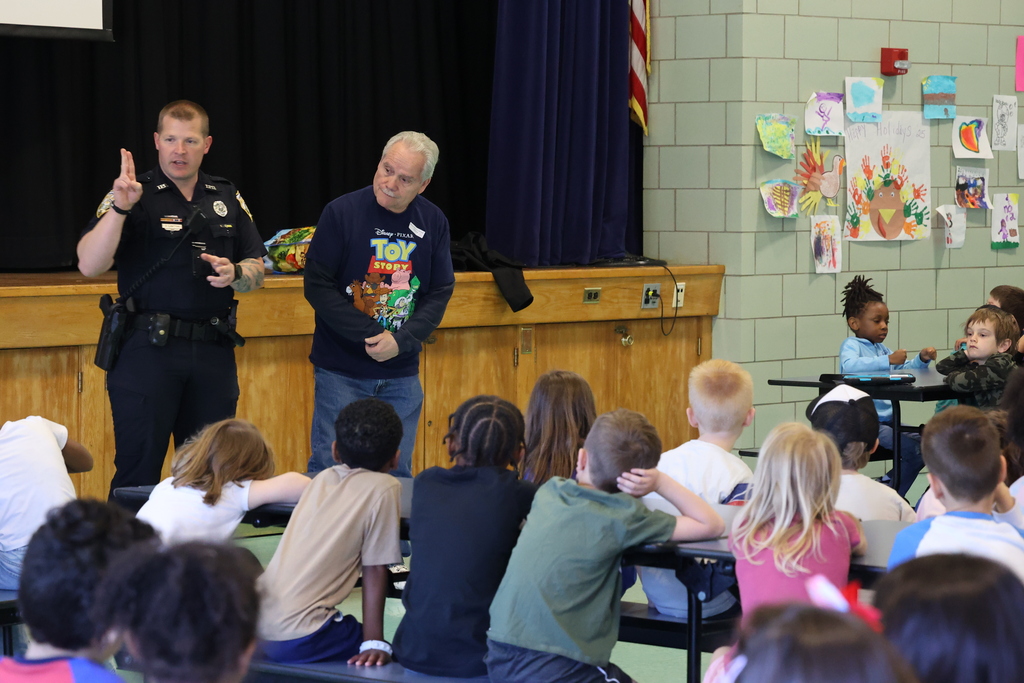 Students listen to a presentation about safety and look at police officer 