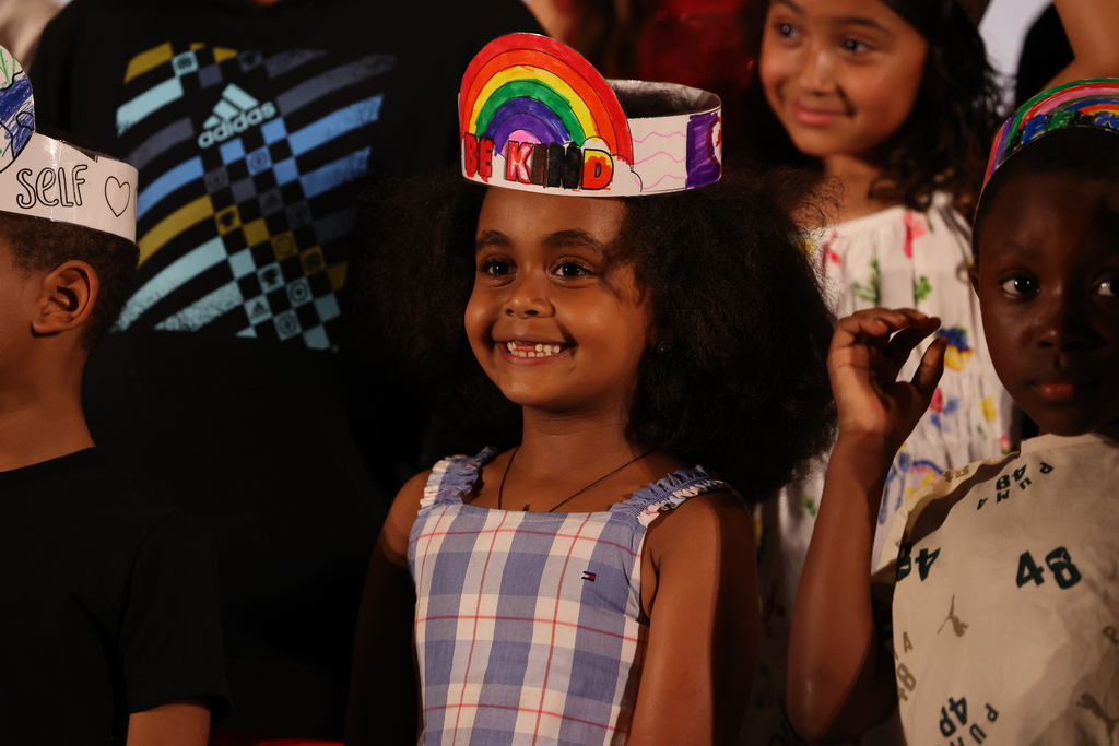 student smiles on stage with missing teeth and be kind crown