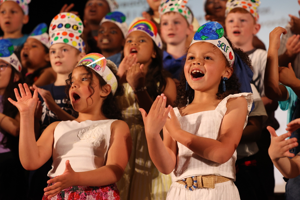 Students sing on stage while doing moves with their hands