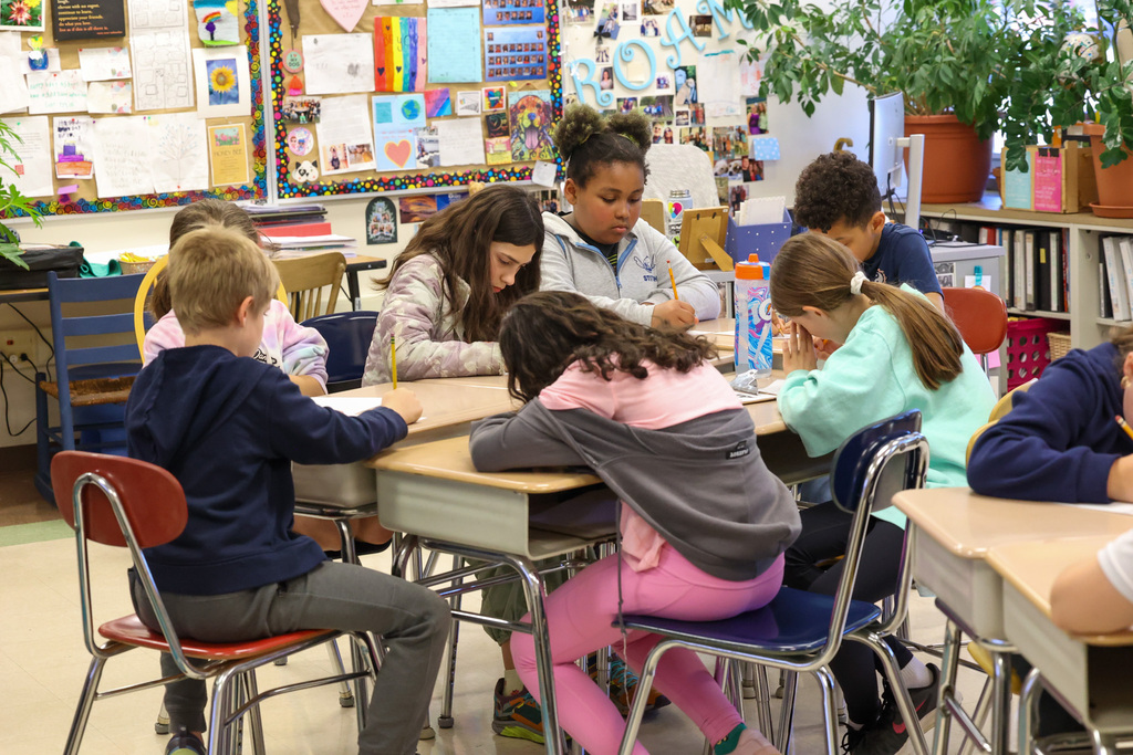 a group of students sit at desks with pencil and papers working on writing assignment in classroom