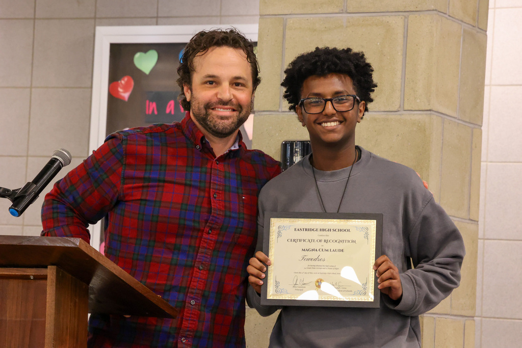 student and staff member smile and pose for the camera with certificate of recognition