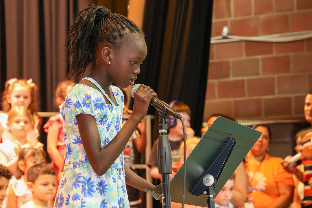 student talks into microphone in a blue flower dress 
