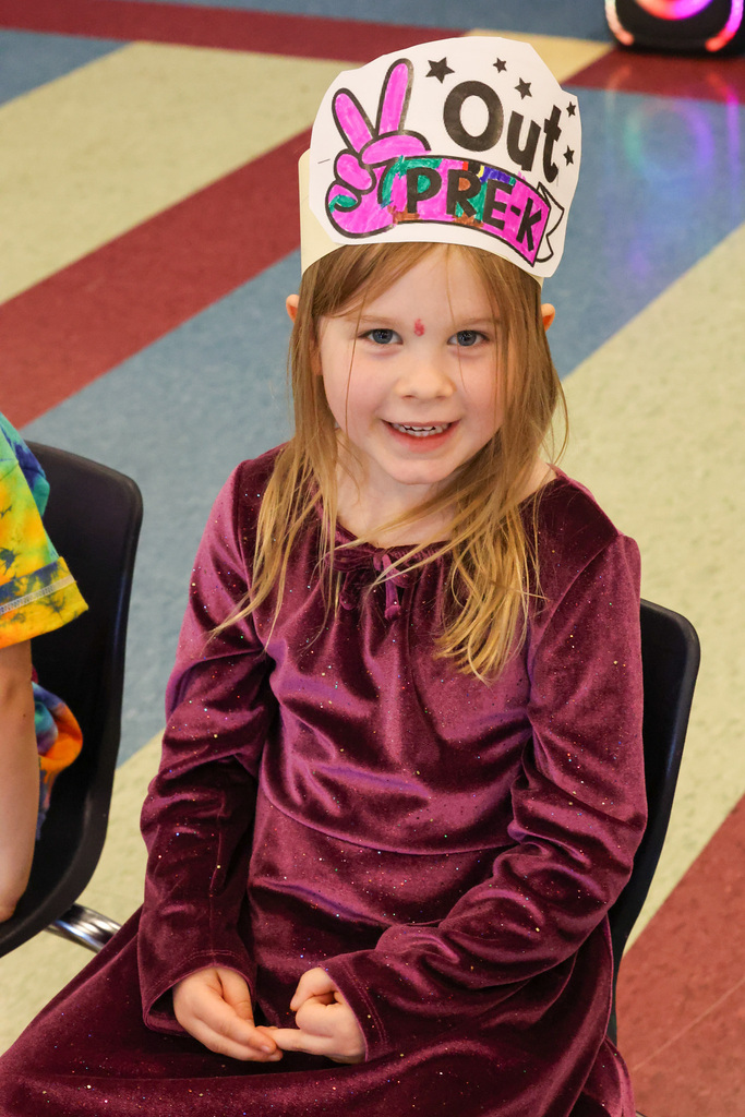 student smiles while sitting in chair with peace out pre k crown