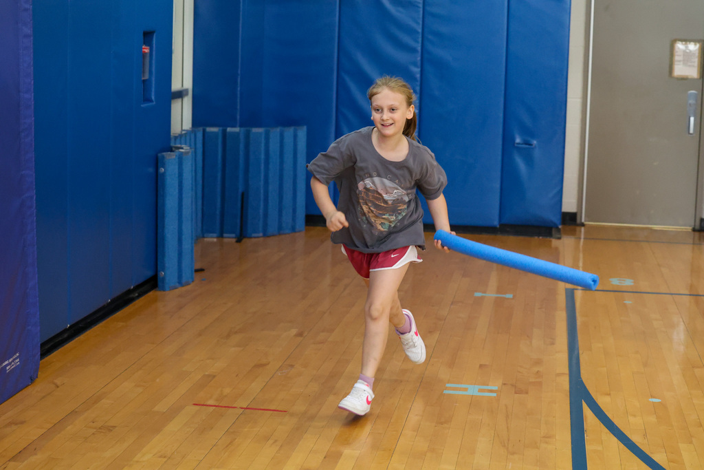 student runs in gym with pool noodle