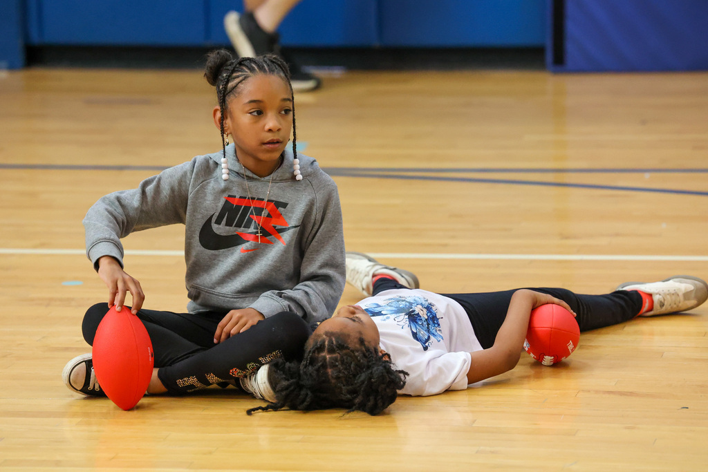 students sit on the ground with footballs