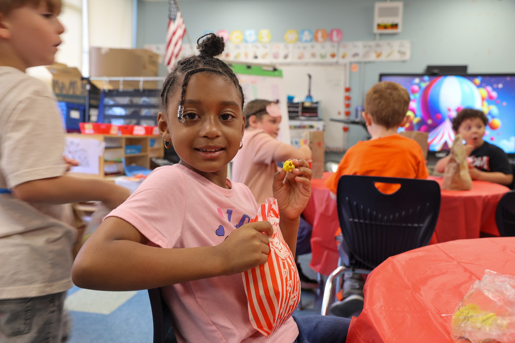 student holds up popcorn and bag while sitting at a table
