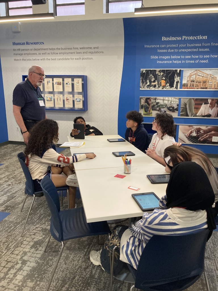 Students work with staff member on field trip at a table with tablets