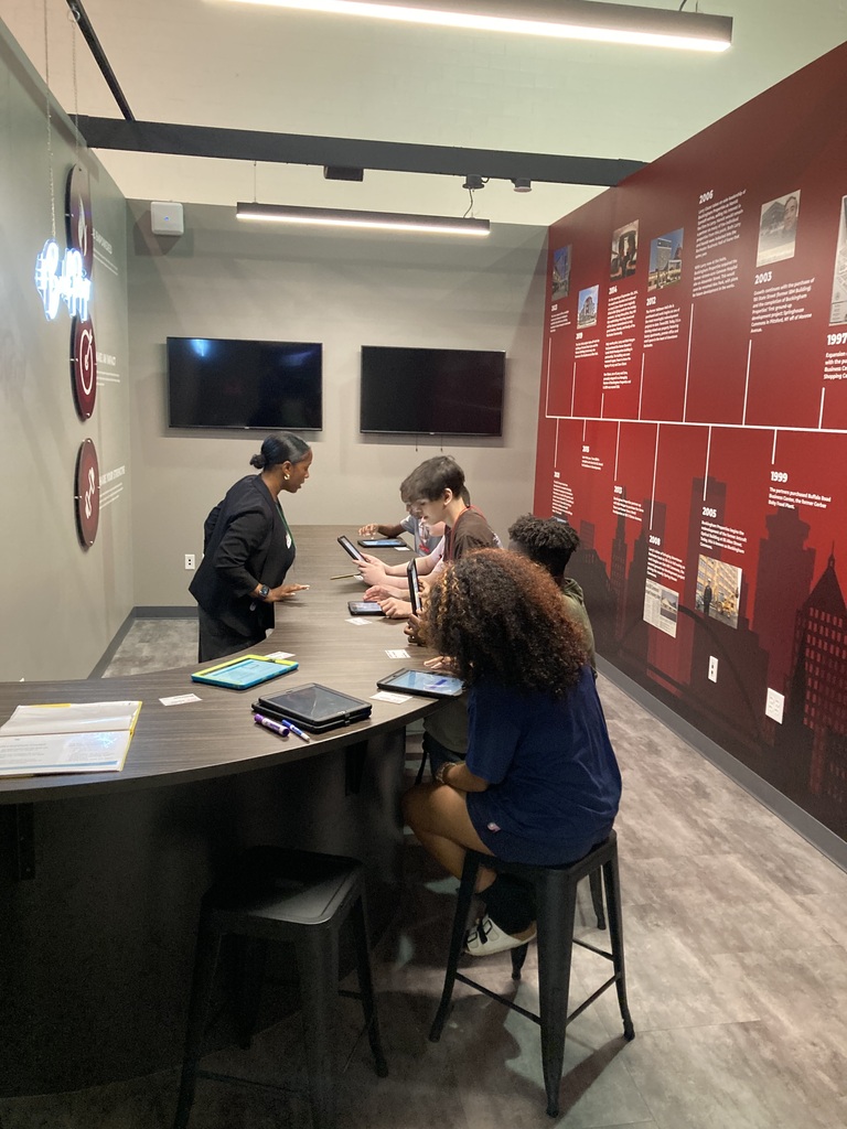 Students work with staff member on field trip at a table with tablets