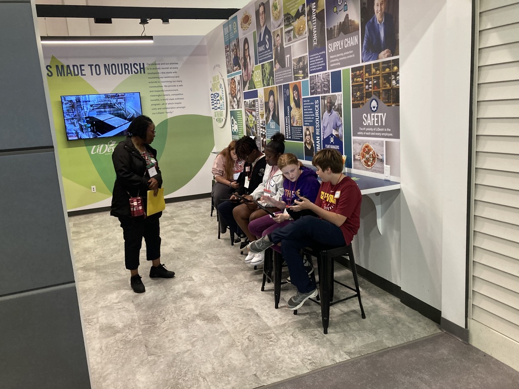 Students work with staff member on field trip at a table with tablets