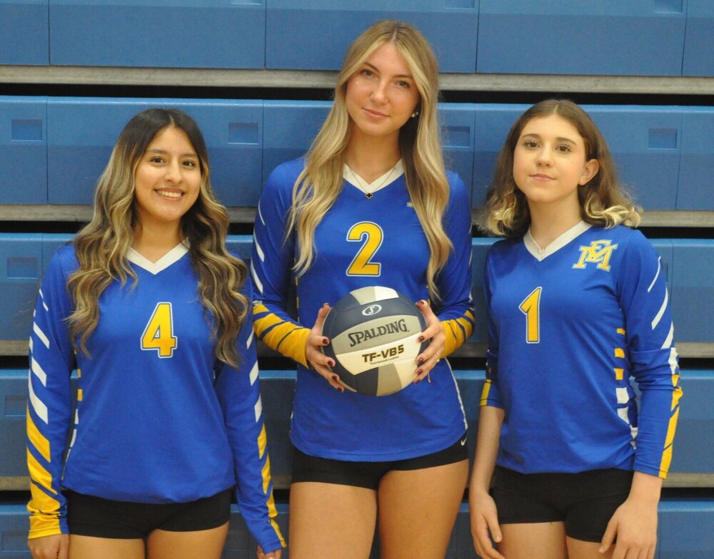 Three student volleyball players smiling, with the center player holding a volleyball.