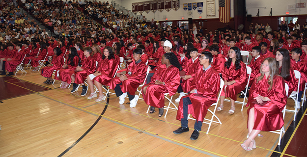 Graduating students in gowns sitting in auditorium.