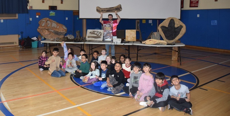 A teacher holds a large fossil above his head in a school gym