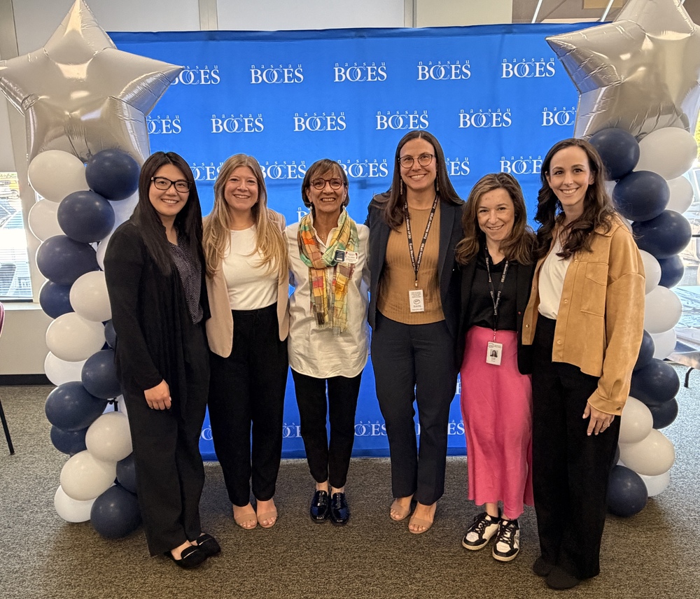 Group of six women posing together in front of a BOES backdrop with balloons and stars, celebrating a special event or achievement.