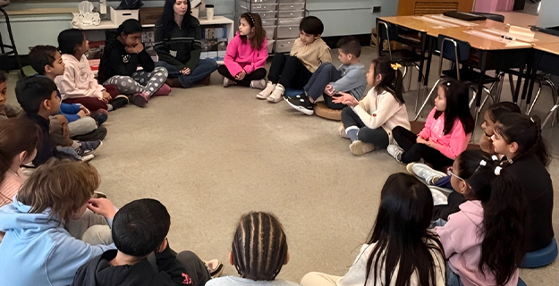 Students sitting in circle on classroom floor.