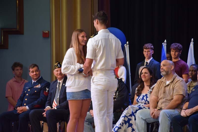 Photo of students receiving American flags from local veterans on stage.