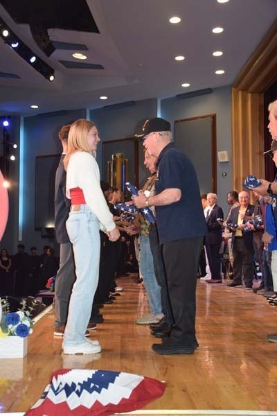 Photo of students receiving American flags from local veterans on stage.