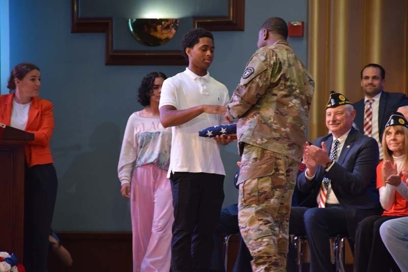 Photo of students receiving American flags from local veterans on stage.