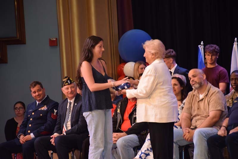 Photo of students receiving American flags from local veterans on stage.