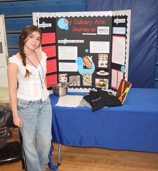Photo of one high school student standing next to poster boards that she created depicting their future careers for their Senior Project Fair.