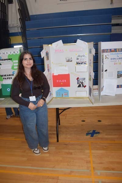 Photo of one high school student standing next to poster boards that she created depicting their future careers for their Senior Project Fair.