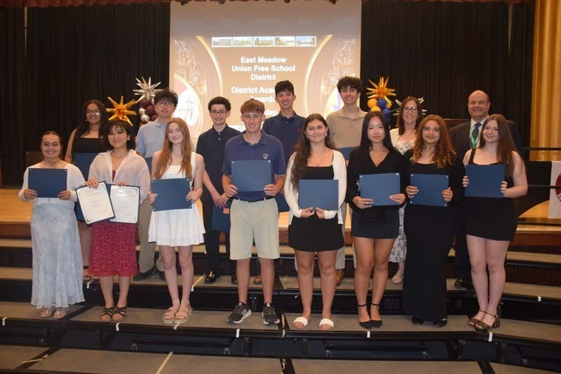 Photo of students standing on risers while holding certificates, medals and awards for their excellence in academics, athletics, clubs and community service.