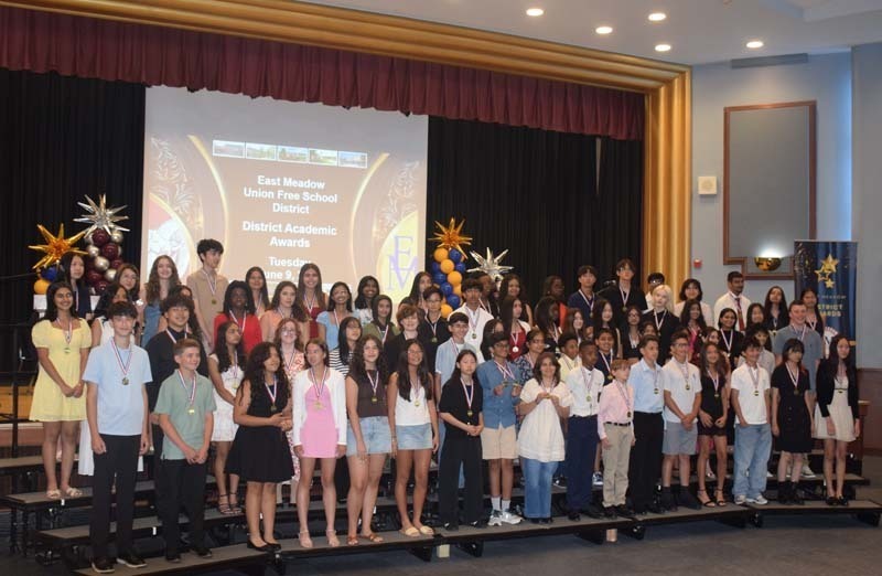 Photo of students standing on risers while holding certificates, medals and awards for their excellence in academics, athletics, clubs and community service.